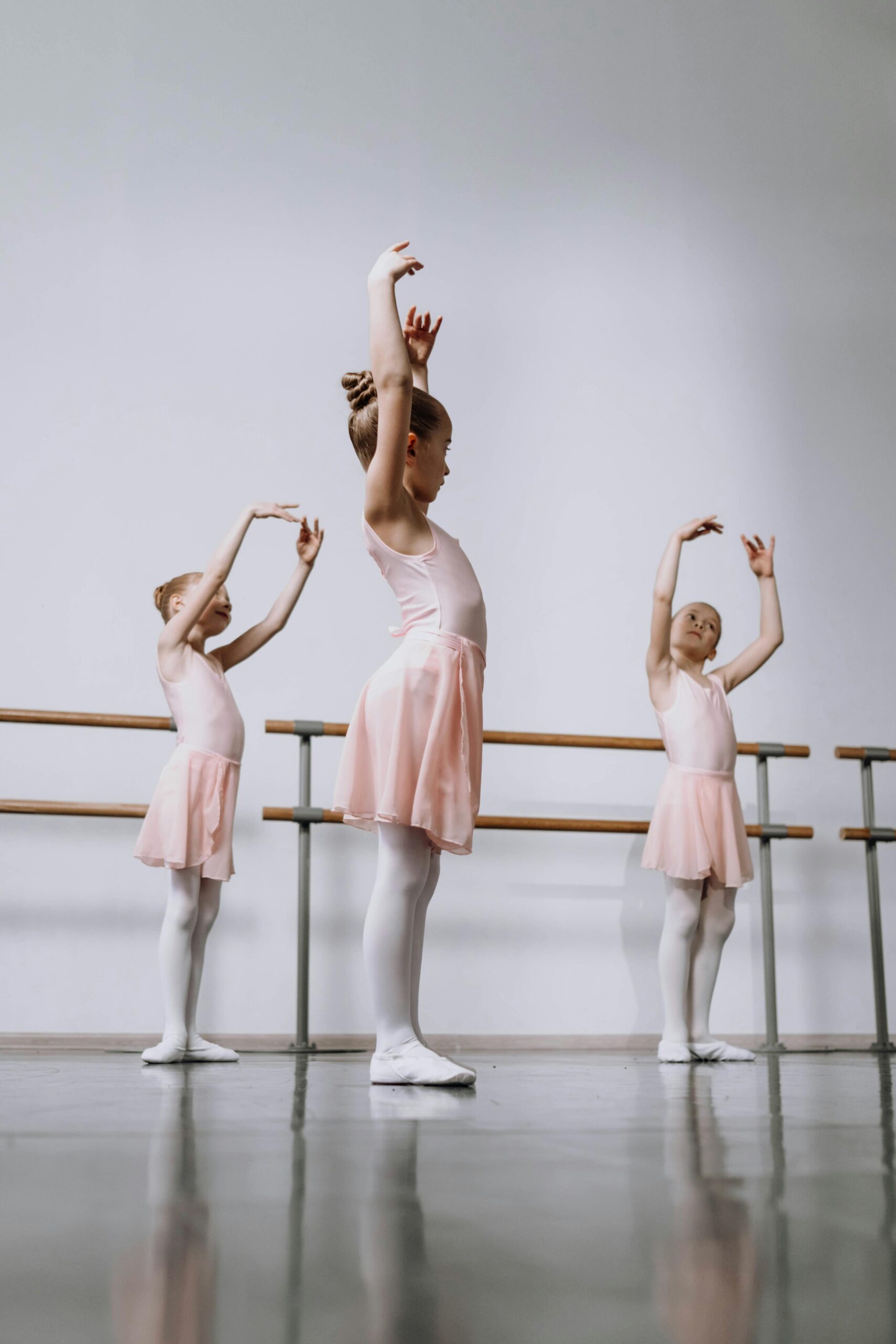 Three young girls practice ballet positions in a dance studio, showcasing grace and technique.